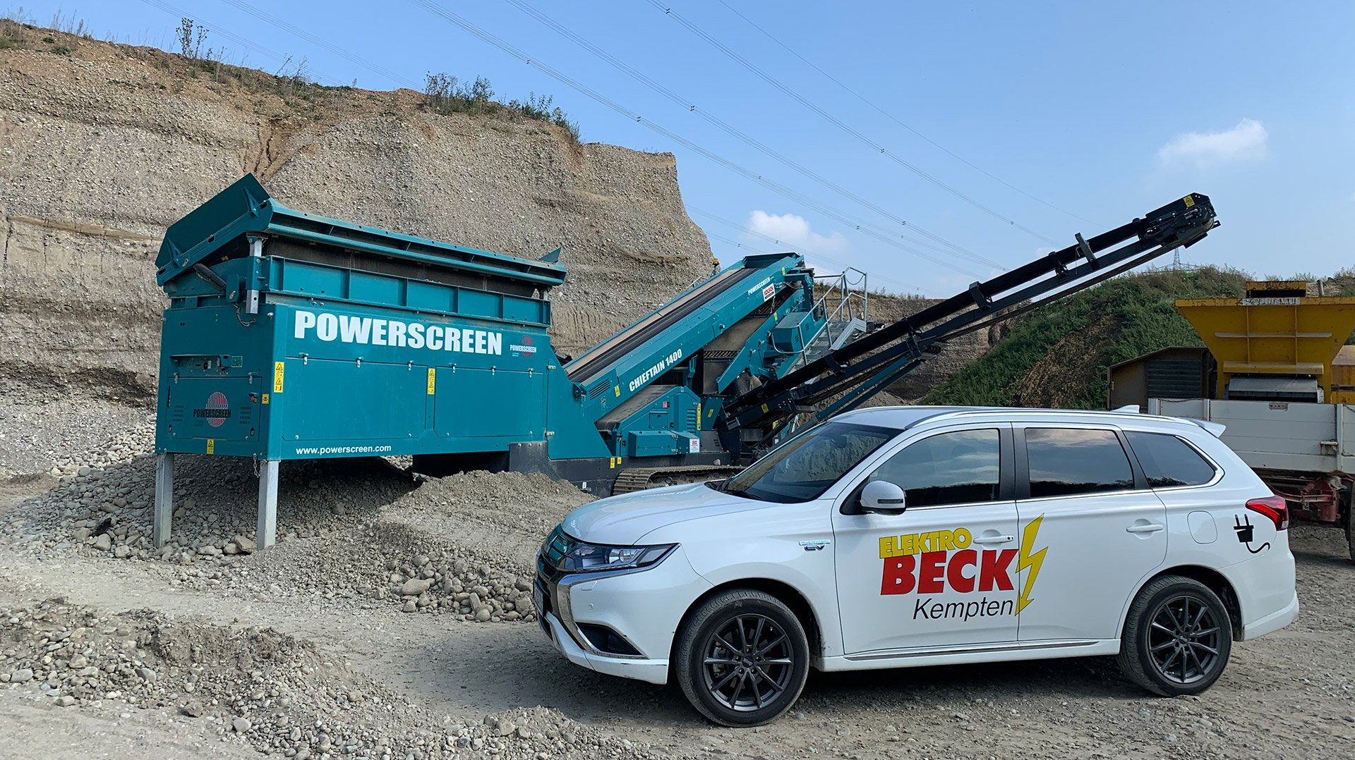 Ein weißes Auo mit dem Elektro Beck Logo vor einer Kießgrube